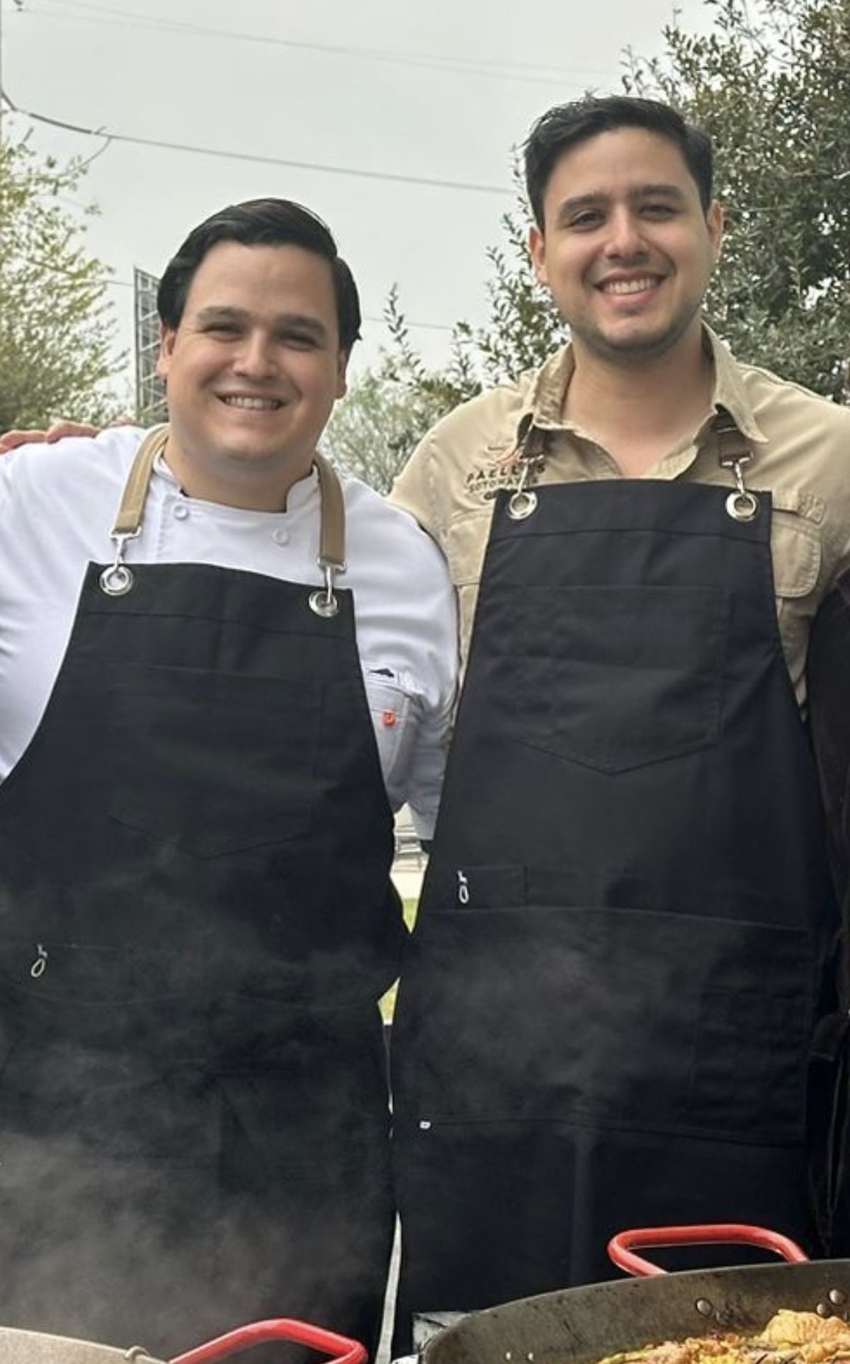 Rodrigo y Luis Sotomayor, fundadores de AUPA, con mandil frente a dos paelleras en Paellas Sotomayor