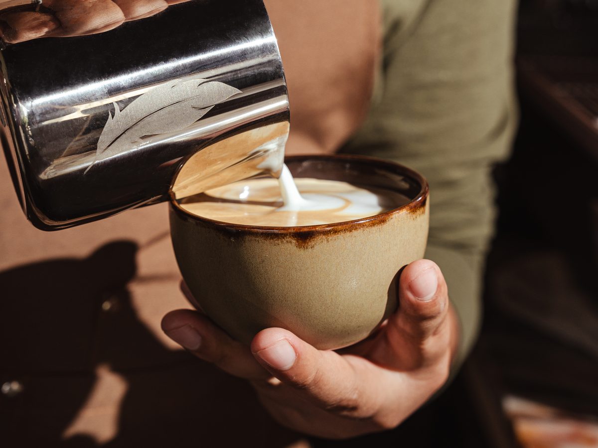 Barista de AUPA vertiendo leche para hacer arte latte en una taza de cerámica